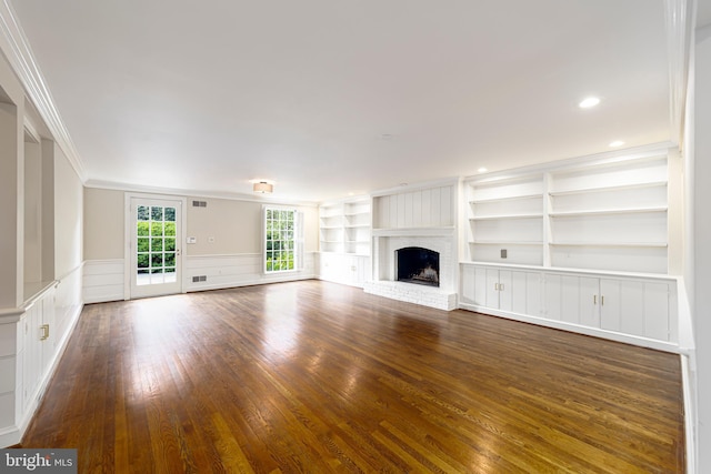 unfurnished living room with a wainscoted wall, dark wood-type flooring, built in features, ornamental molding, and a brick fireplace