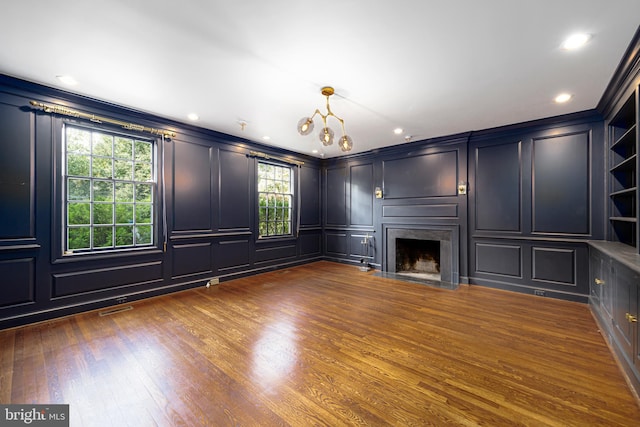 unfurnished living room featuring a decorative wall, a fireplace, visible vents, dark wood finished floors, and crown molding