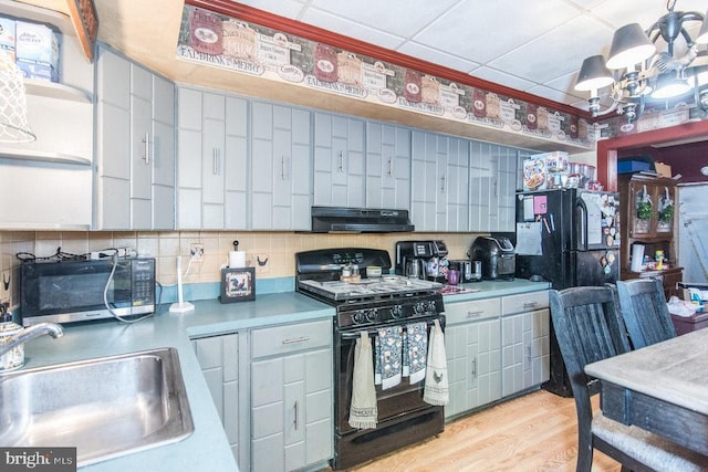 kitchen with sink, tasteful backsplash, a notable chandelier, black appliances, and light wood-type flooring