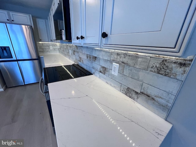 kitchen featuring electric stove, wood-type flooring, stainless steel refrigerator with ice dispenser, light stone counters, and tasteful backsplash