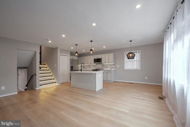 kitchen featuring light wood-type flooring, an island with sink, pendant lighting, and stainless steel appliances