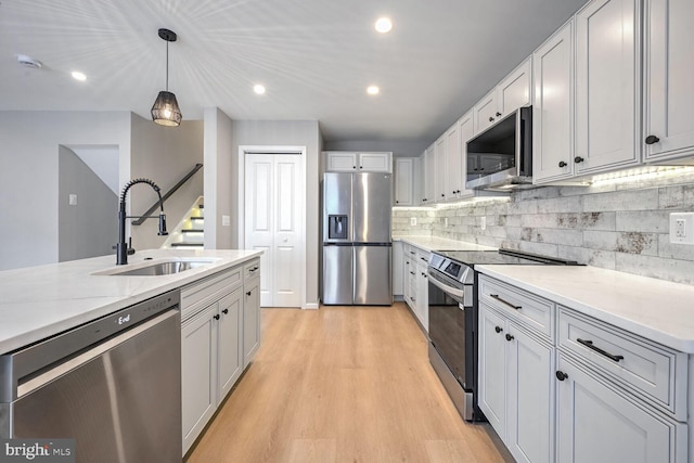 kitchen featuring appliances with stainless steel finishes, light stone countertops, light hardwood / wood-style floors, pendant lighting, and sink