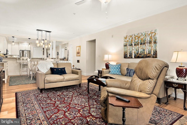 living room with ornamental molding, ceiling fan with notable chandelier, and light hardwood / wood-style flooring