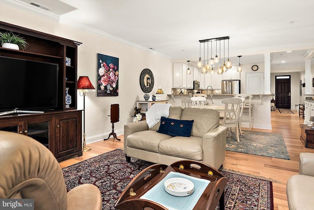 living room featuring sink, crown molding, and light hardwood / wood-style flooring