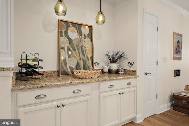 bar with hanging light fixtures, white cabinets, light stone counters, and light hardwood / wood-style floors