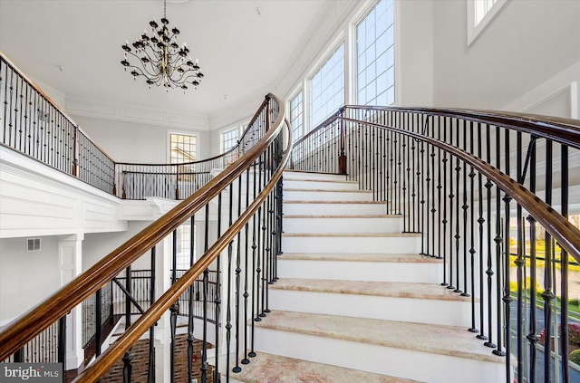 staircase featuring a towering ceiling, ornamental molding, and a notable chandelier