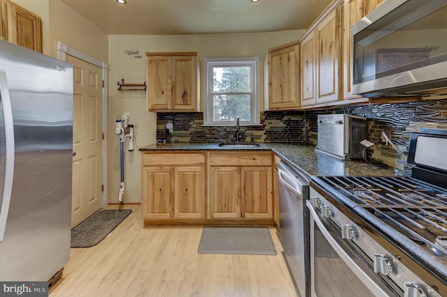 kitchen featuring appliances with stainless steel finishes, light brown cabinetry, sink, backsplash, and dark stone counters