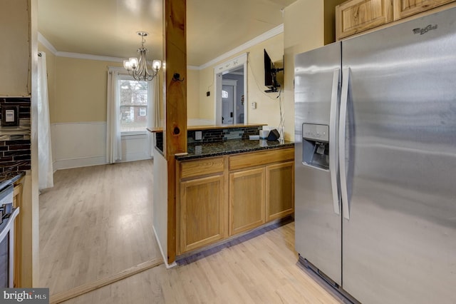 kitchen with crown molding, stainless steel refrigerator with ice dispenser, decorative light fixtures, dark stone counters, and light wood-type flooring