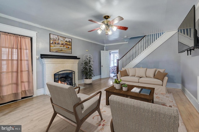 living room featuring a fireplace, light hardwood / wood-style flooring, ornamental molding, and ceiling fan