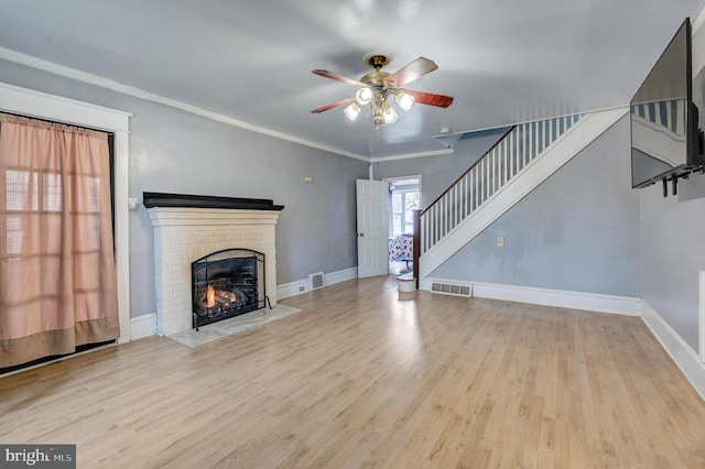 unfurnished living room with ornamental molding, a brick fireplace, ceiling fan, and light hardwood / wood-style floors