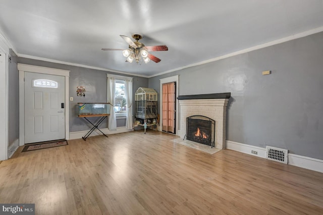 unfurnished living room featuring crown molding, ceiling fan, a fireplace, and light wood-type flooring