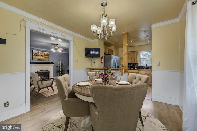 dining area with ornamental molding, sink, ceiling fan with notable chandelier, and light hardwood / wood-style floors