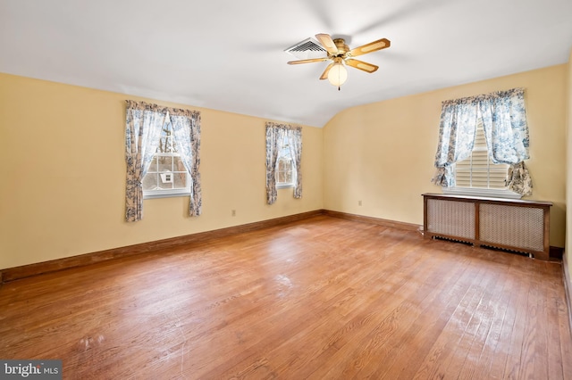 empty room featuring hardwood / wood-style flooring, ceiling fan, radiator heating unit, and vaulted ceiling