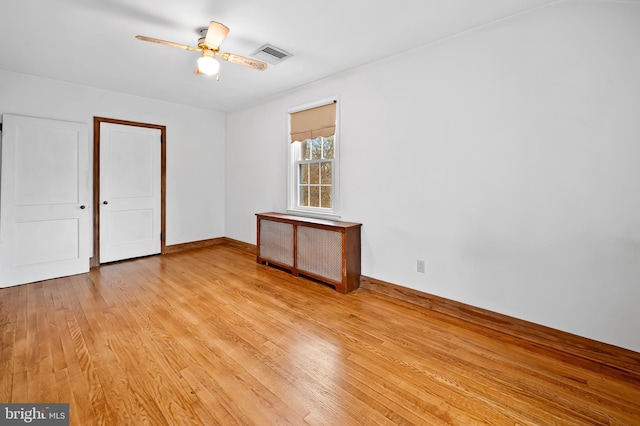 spare room featuring ceiling fan, radiator heating unit, and light wood-type flooring