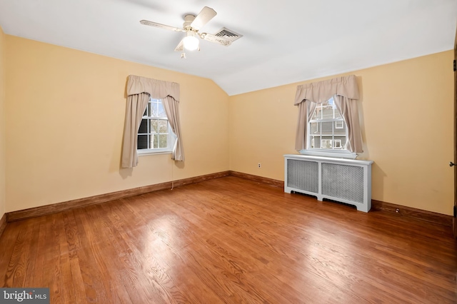 empty room featuring wood-type flooring, lofted ceiling, radiator heating unit, and ceiling fan