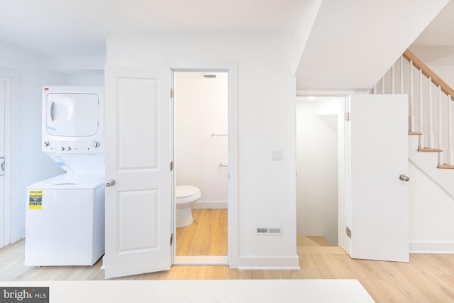 laundry area featuring light wood finished floors, baseboards, visible vents, and stacked washer and clothes dryer