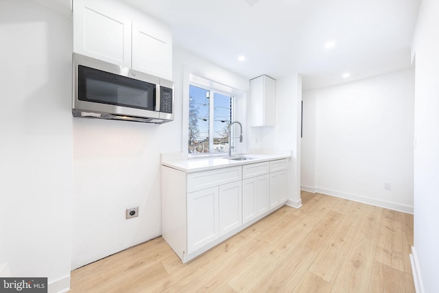 kitchen with white cabinetry, stainless steel microwave, light countertops, and a sink