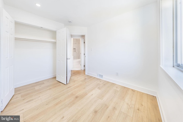 unfurnished bedroom featuring light wood-style flooring, a closet, visible vents, and baseboards