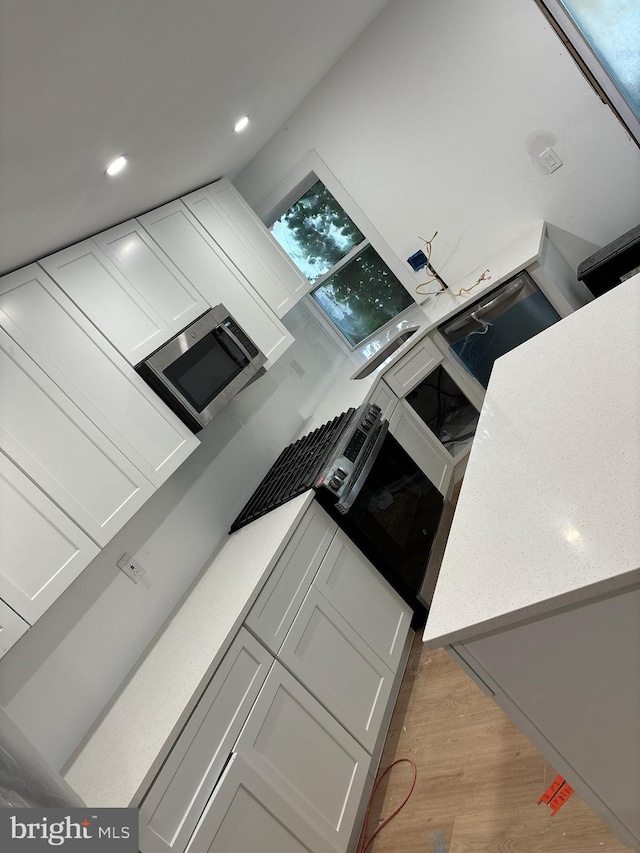 kitchen featuring light wood finished floors, recessed lighting, light countertops, stainless steel microwave, and white cabinets