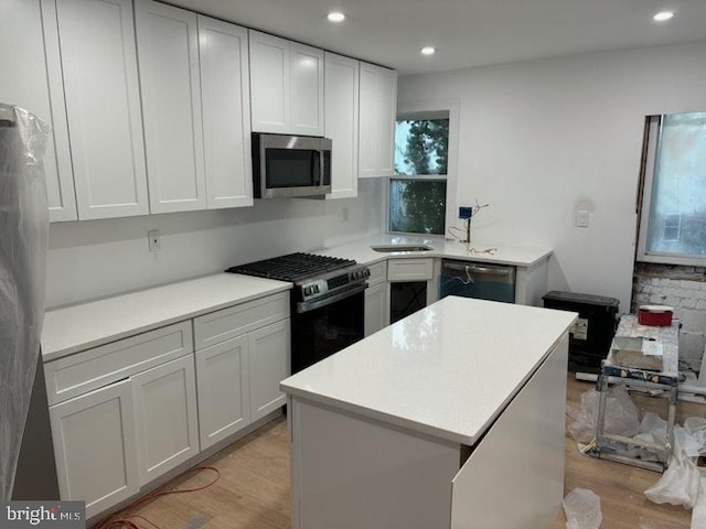 kitchen with a kitchen island, light hardwood / wood-style flooring, white cabinets, and appliances with stainless steel finishes