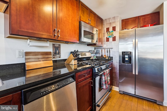 kitchen featuring stainless steel appliances, dark stone counters, and light wood-type flooring