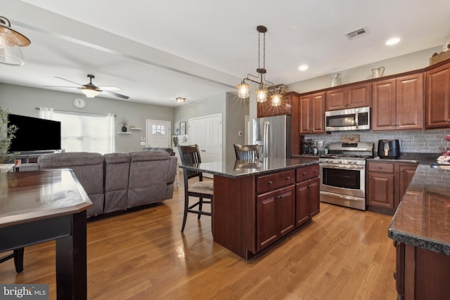 kitchen with pendant lighting, appliances with stainless steel finishes, backsplash, wood-type flooring, and a kitchen island