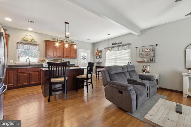 living room with sink, beamed ceiling, and light wood-type flooring