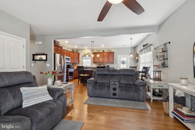 living room featuring sink, lofted ceiling with beams, light hardwood / wood-style floors, and ceiling fan