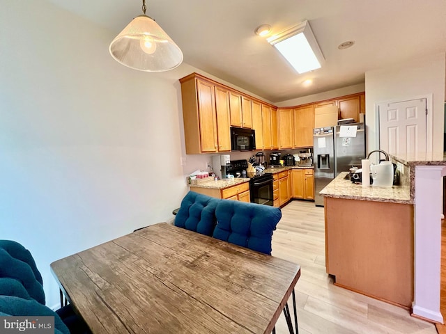 kitchen featuring decorative light fixtures, light hardwood / wood-style flooring, light stone counters, and black appliances