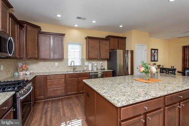 kitchen featuring sink, dark wood-type flooring, stainless steel appliances, light stone counters, and a kitchen island