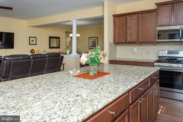 kitchen with appliances with stainless steel finishes, tasteful backsplash, light stone counters, dark hardwood / wood-style flooring, and ornate columns