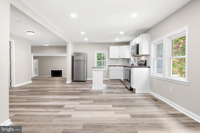 kitchen featuring appliances with stainless steel finishes, white cabinets, light hardwood / wood-style floors, and decorative backsplash