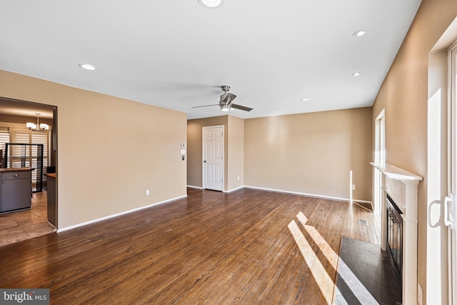 unfurnished living room with ceiling fan with notable chandelier and dark wood-type flooring