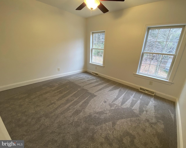 unfurnished room featuring dark colored carpet, a wealth of natural light, and ceiling fan