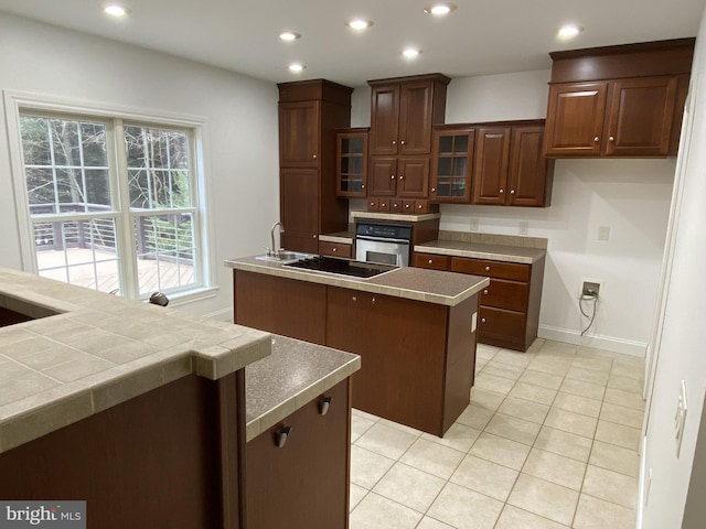 kitchen featuring dark brown cabinets, light tile patterned floors, black electric cooktop, an island with sink, and oven