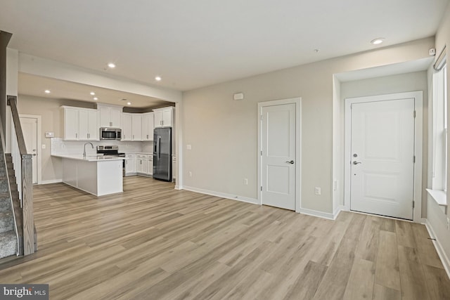 kitchen with light wood-style flooring, stainless steel appliances, a peninsula, white cabinets, and open floor plan