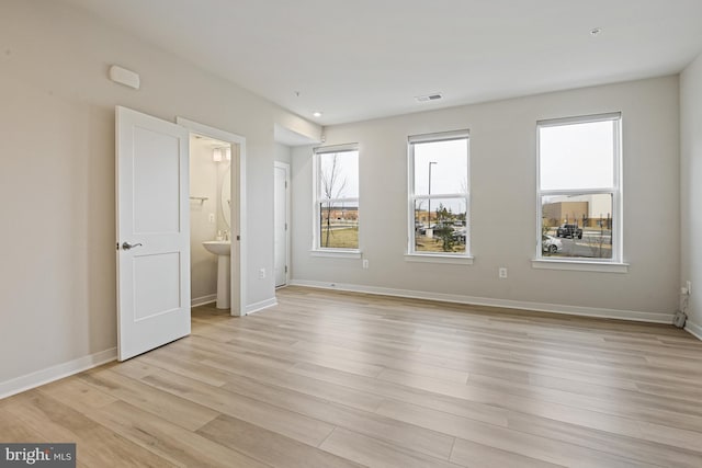 unfurnished bedroom with baseboards, connected bathroom, visible vents, and light wood finished floors