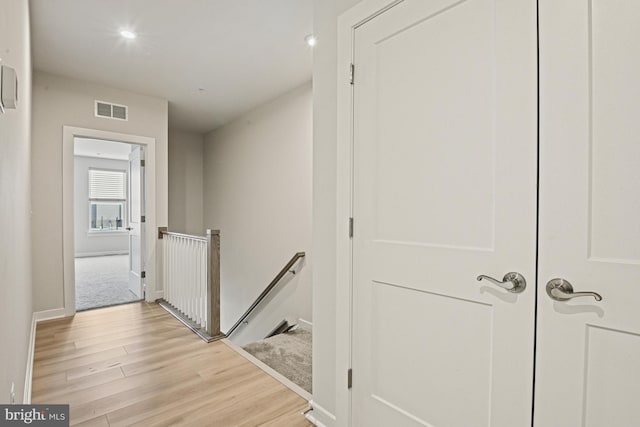 hallway with recessed lighting, visible vents, light wood finished floors, and an upstairs landing