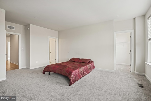 bedroom with carpet, a walk in closet, visible vents, and baseboards