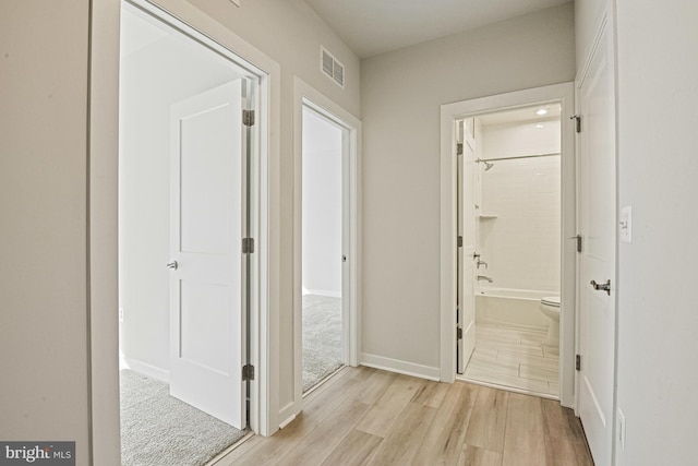 hallway with light wood finished floors, visible vents, and baseboards