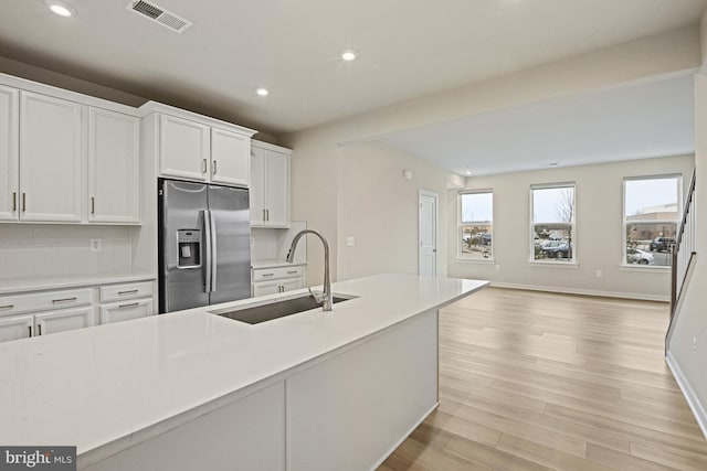 kitchen featuring stainless steel refrigerator with ice dispenser, light countertops, visible vents, white cabinets, and a sink