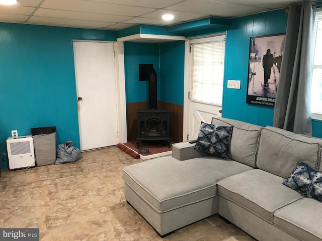 living room with a paneled ceiling, wood walls, and a wood stove