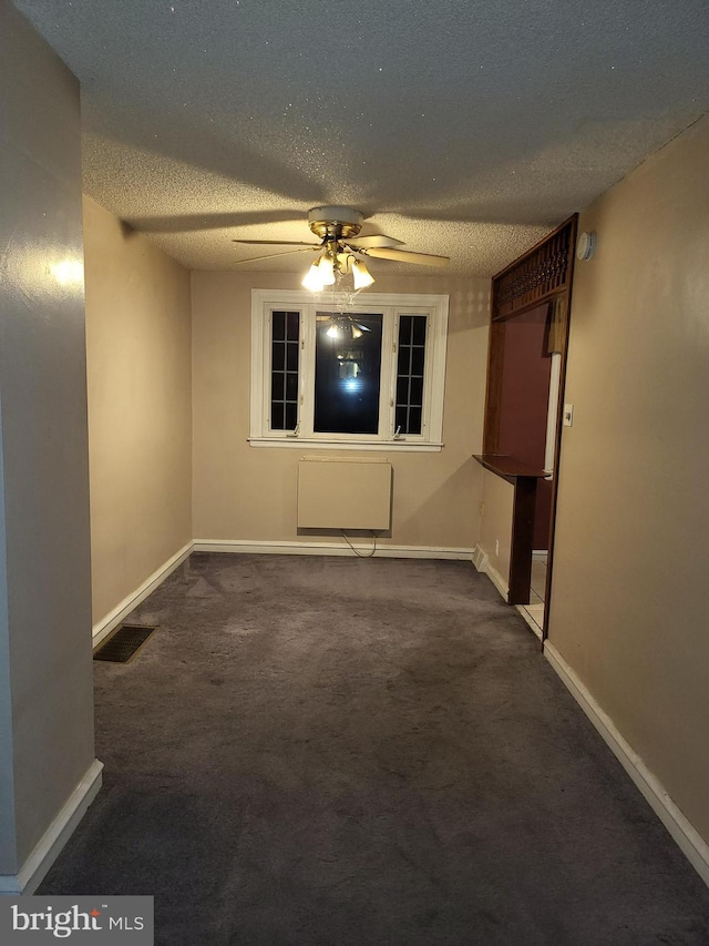 spare room with dark colored carpet, ceiling fan, and a textured ceiling