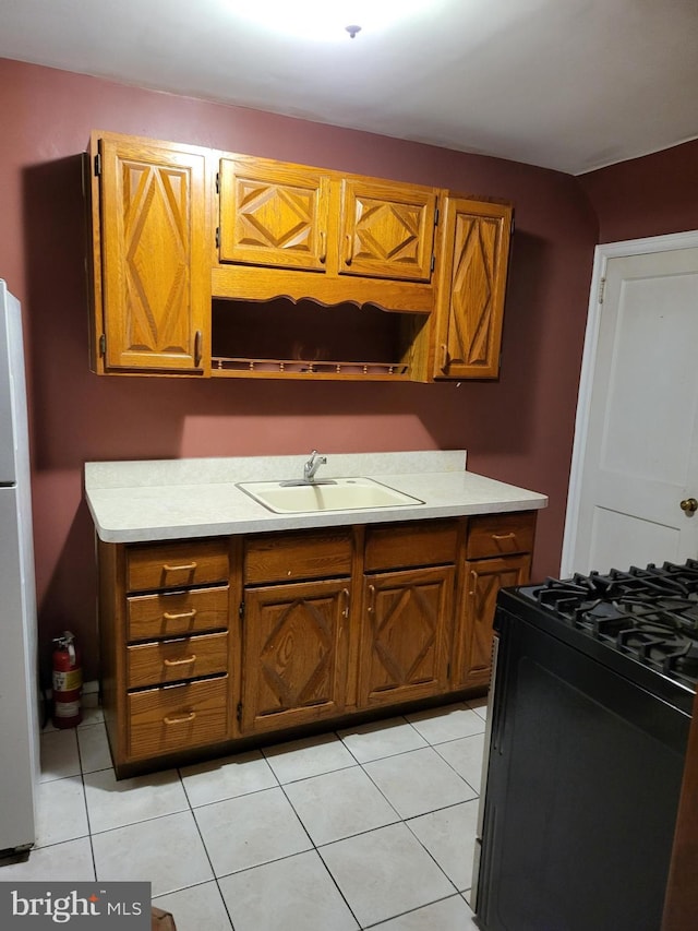 kitchen featuring white refrigerator, sink, range with gas cooktop, and light tile patterned floors