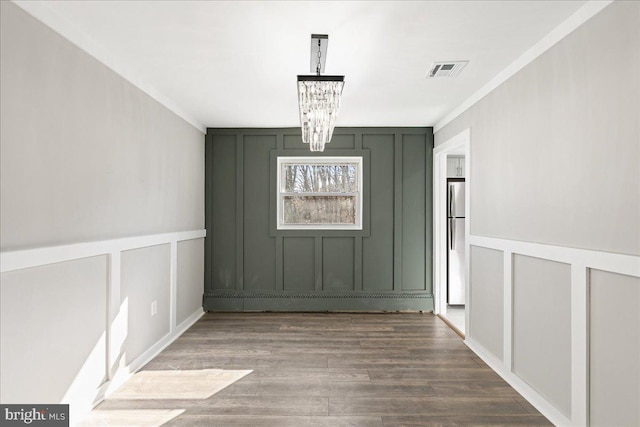 unfurnished dining area featuring a notable chandelier, visible vents, a decorative wall, ornamental molding, and wood finished floors