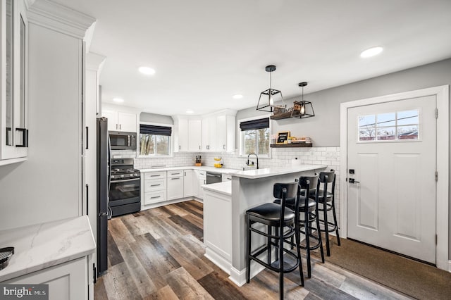 kitchen with appliances with stainless steel finishes, a breakfast bar, white cabinetry, hanging light fixtures, and kitchen peninsula