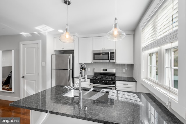 kitchen featuring hanging light fixtures, dark stone counters, stainless steel appliances, decorative backsplash, and white cabinets