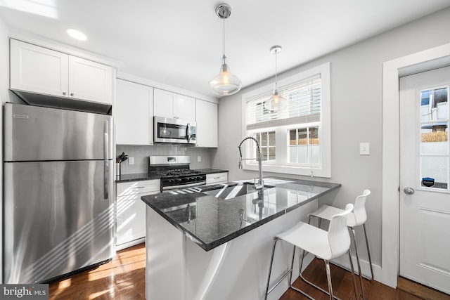 kitchen featuring appliances with stainless steel finishes, decorative light fixtures, white cabinetry, sink, and a kitchen bar