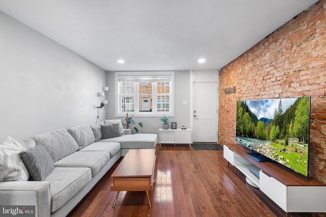 living room featuring dark wood-type flooring and brick wall