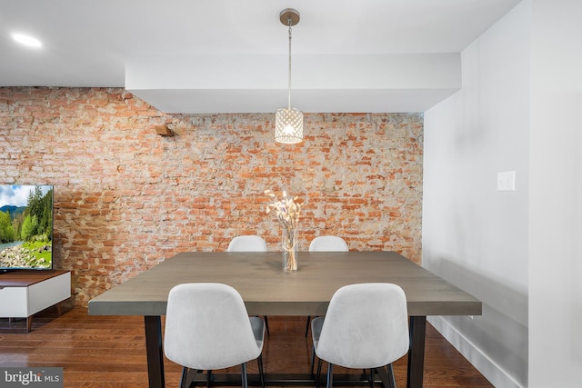 dining area featuring brick wall and dark hardwood / wood-style flooring